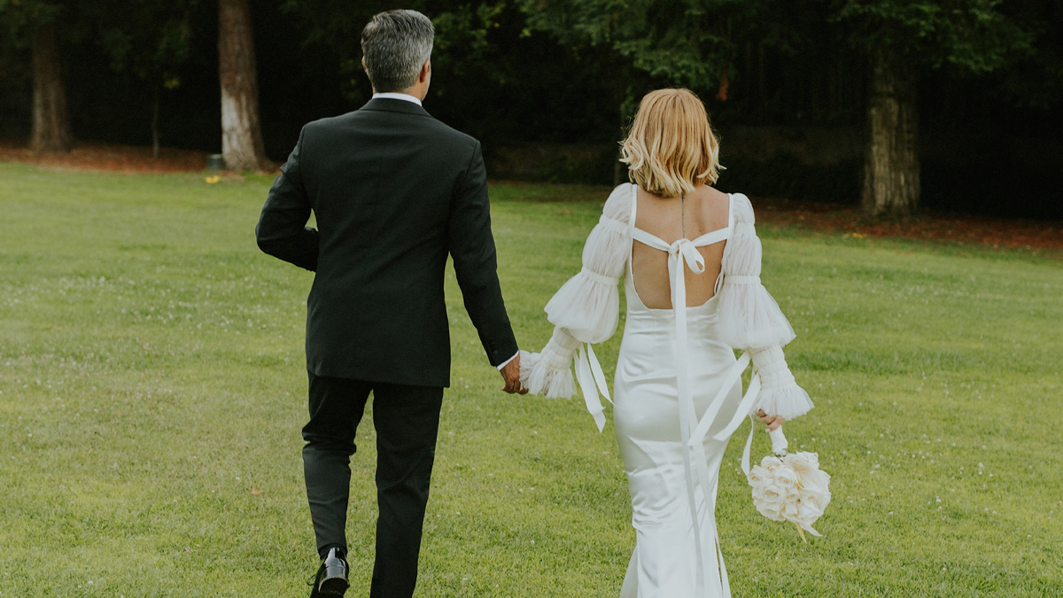 couple walking hand in hand in a field, showcasing the new wedding jewelry collection from CINCO Jewelry
