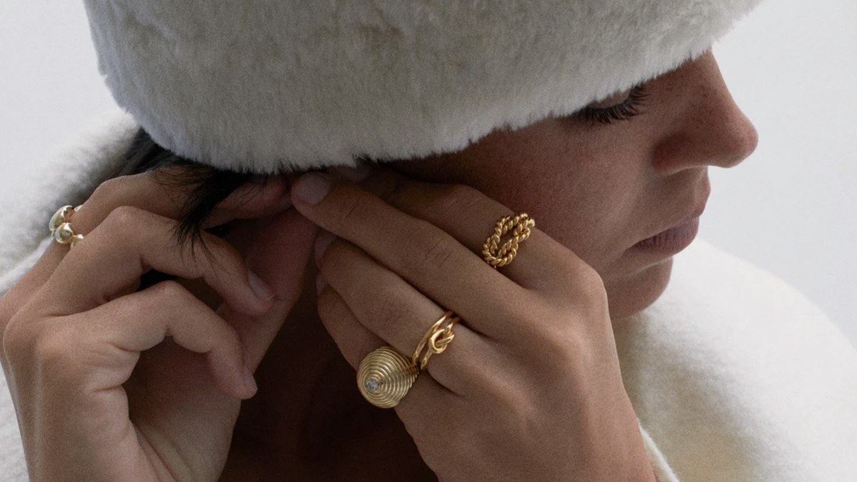 Woman styling her hair while wearing elegant jewelry, highlighting misogyny in fashion design.