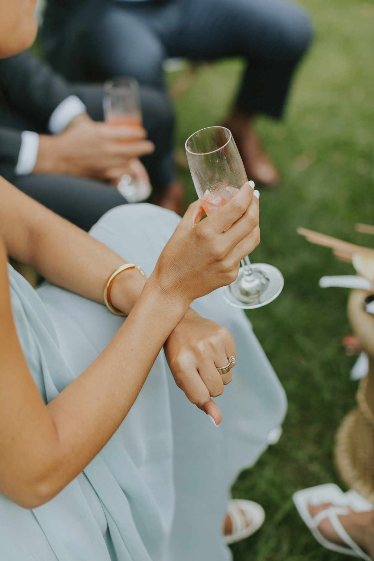 An elegant hand holding a drink, showcasing wedding jewelry metal choice with rings and a beautiful bracelet.