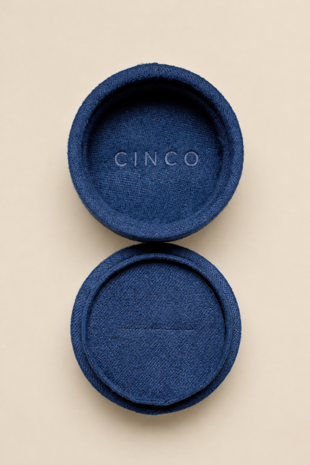 A pair of round blue fabric-covered ring stands or coasters with a woven texture, shown on a light beige background. The top piece is open, revealing the brand name 'CINCO' embossed in the center, and the bottom piece is closed.