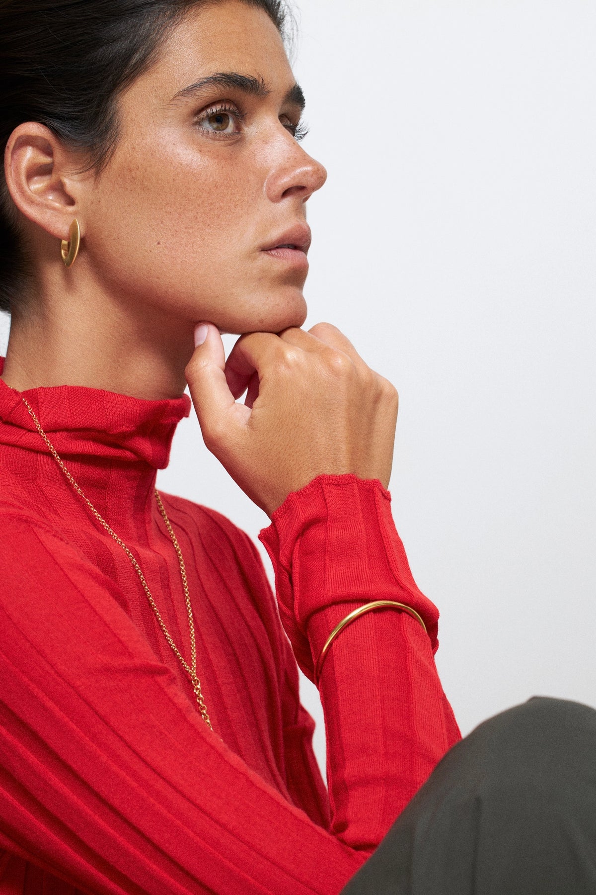 Modelo usando brincos CINCO em formato oval com blusa vermelha, destacando o estilo e detalhe do acessório.