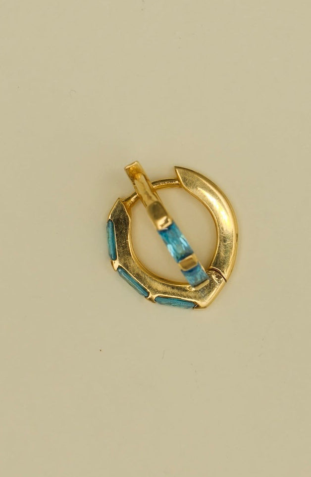 Gold hoop earring with blue gemstones on a beige background