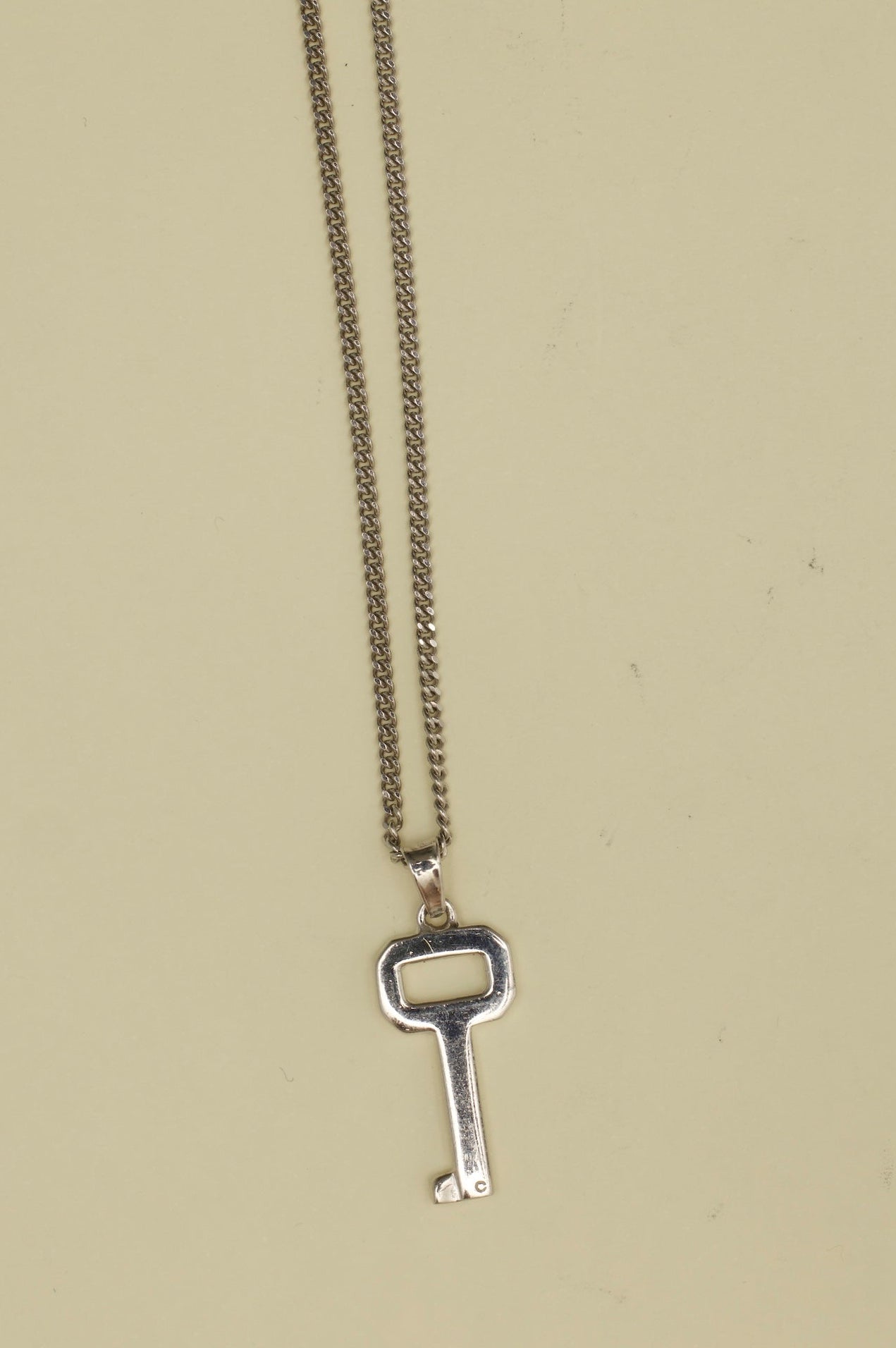 Silver key-shaped pendant on a chain against a beige background
