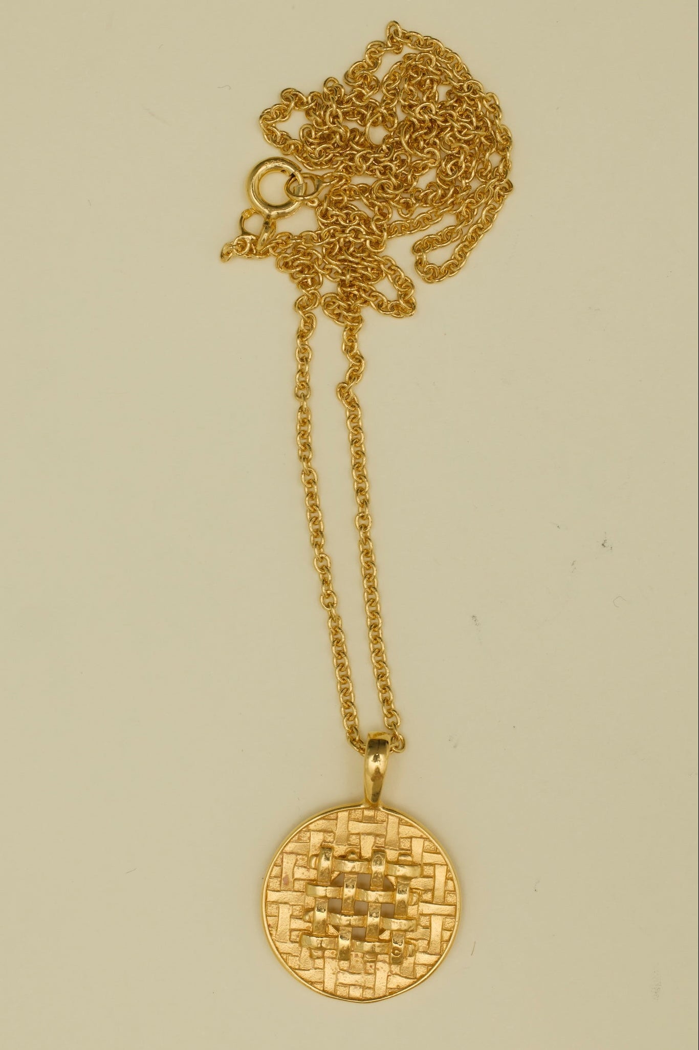 Gold necklace with a round pendant on a beige background
