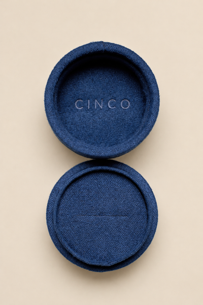 A pair of round blue fabric-covered ring stands or coasters with a woven texture, shown on a light beige background. The top piece is open, revealing the brand name 'CINCO' embossed in the center, and the bottom piece is closed.