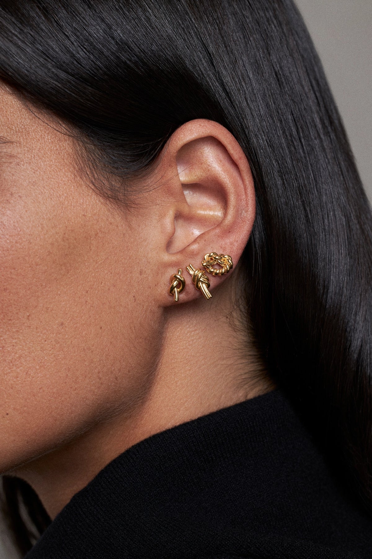 CINCO earrings worn on ear, showcasing gold-tone design with unique detail, modeled on a woman.