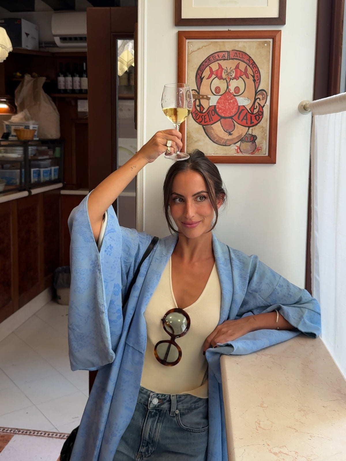 Young woman in blue kimono holding a glass of wine, smiling in a café setting.