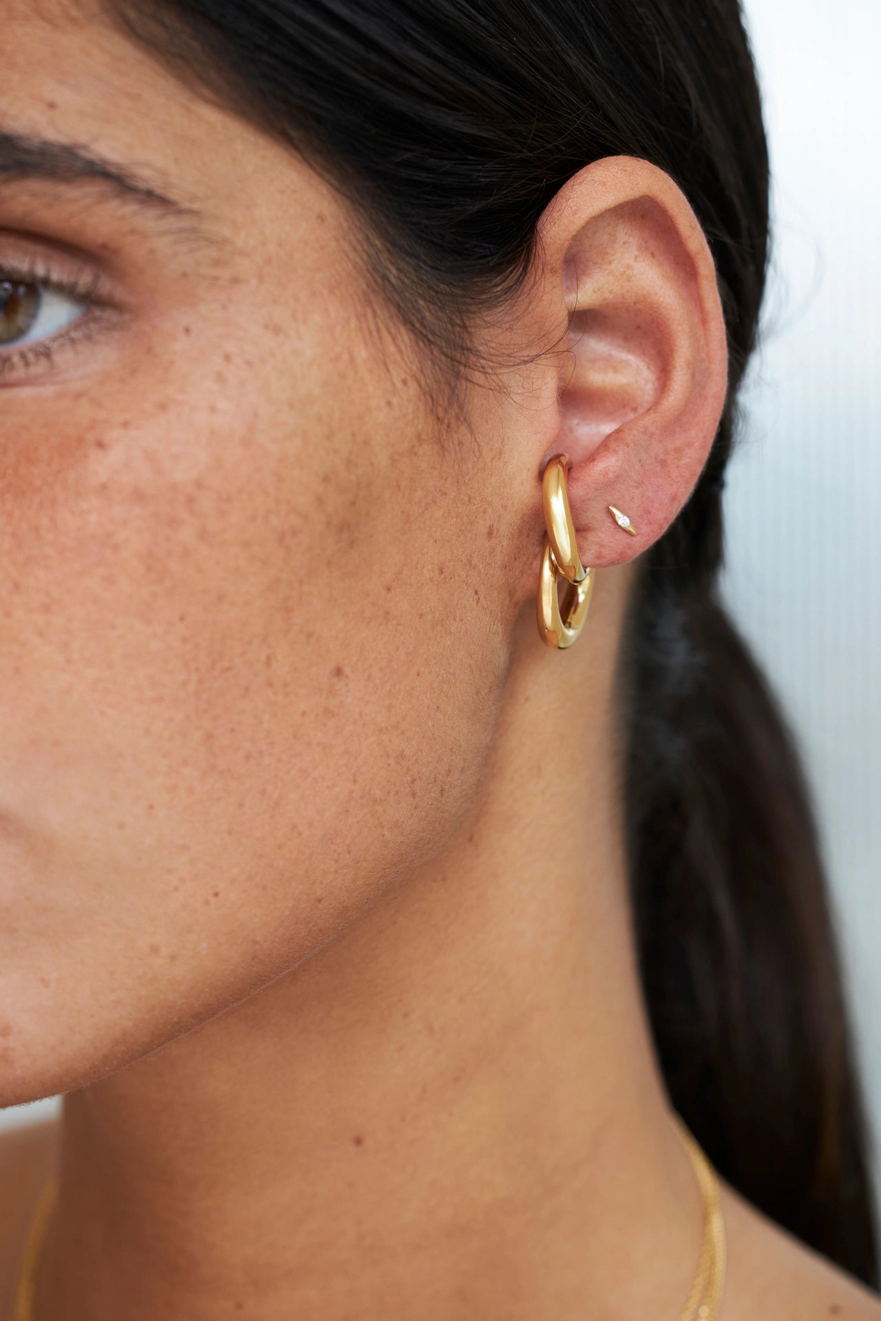 Close-up of a person wearing a gold hoop earring with a blurred background