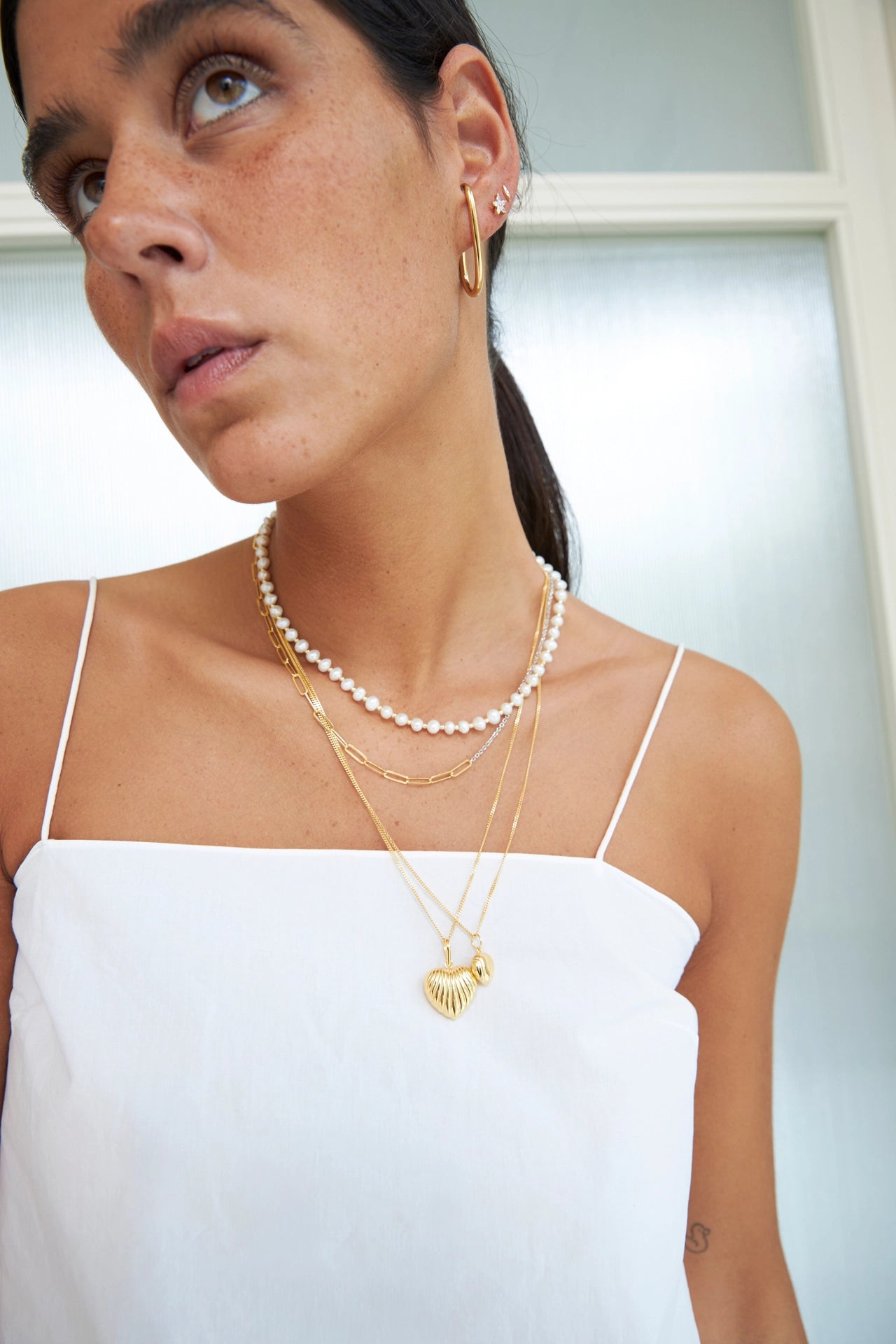 Woman wearing pearl necklace and gold jewelry against a neutral background