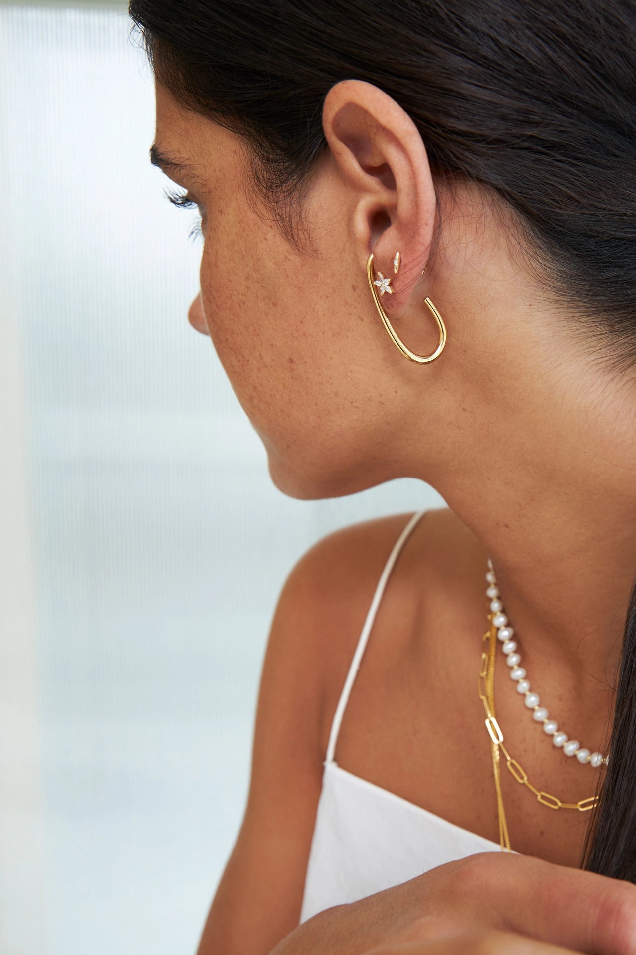 Close-up of a woman wearing gold hoop earrings and a pearl necklace against a blurred background.