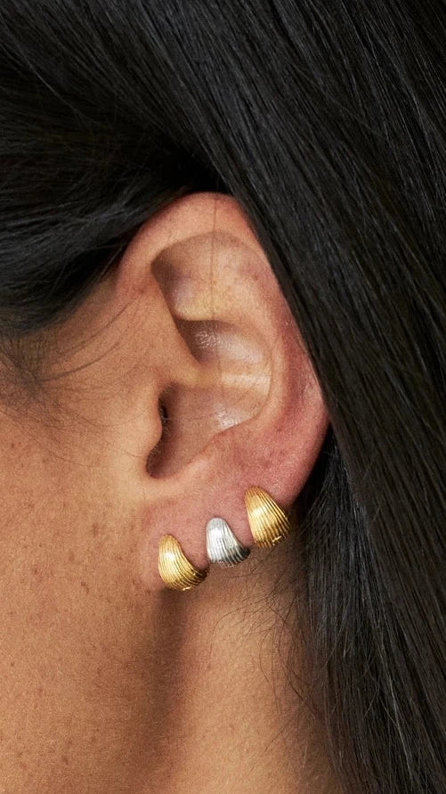 Close-up of a person wearing colorful earrings with a neutral background