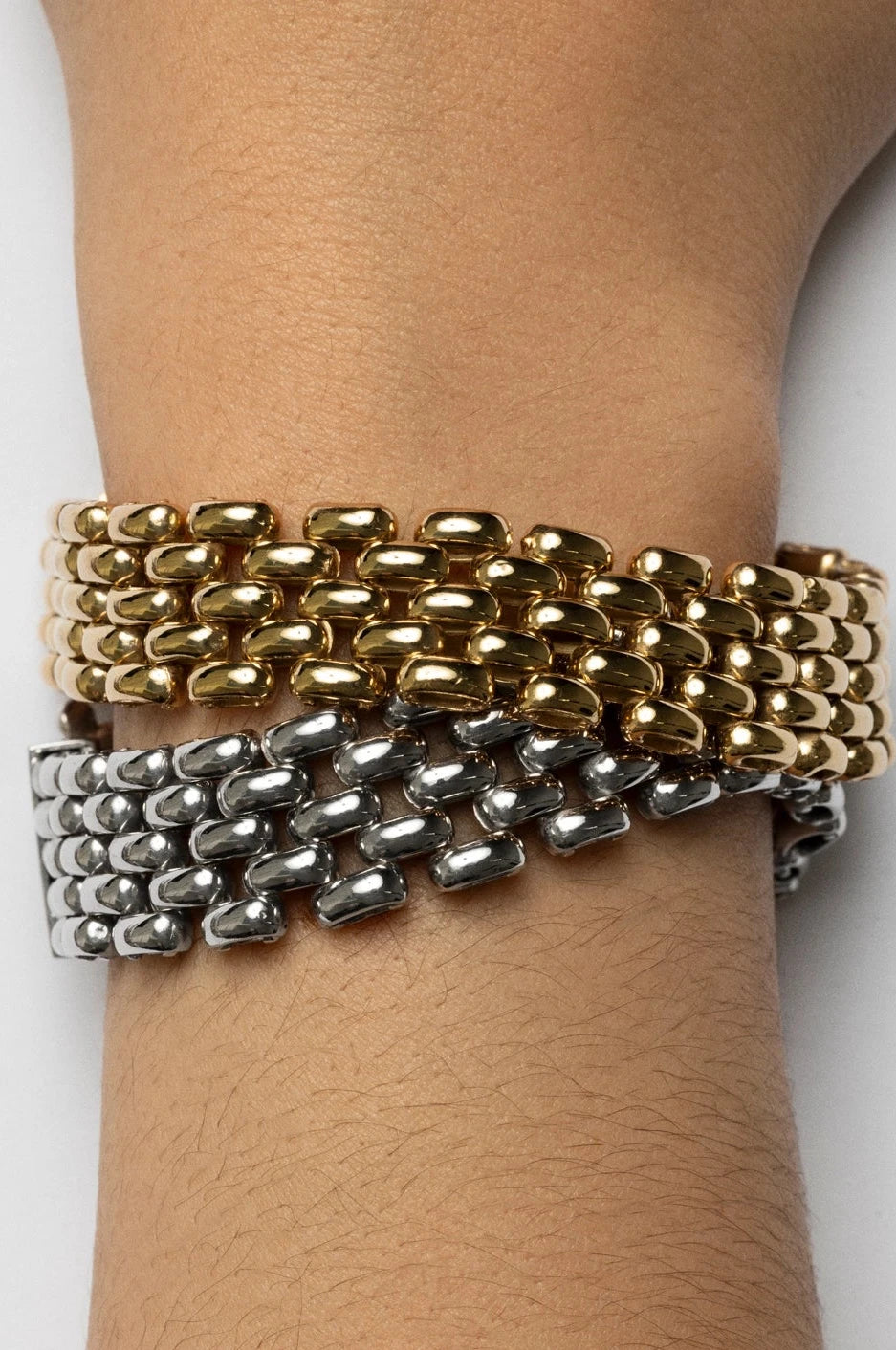 Two bracelets, one gold and one silver, on a wrist against a white background