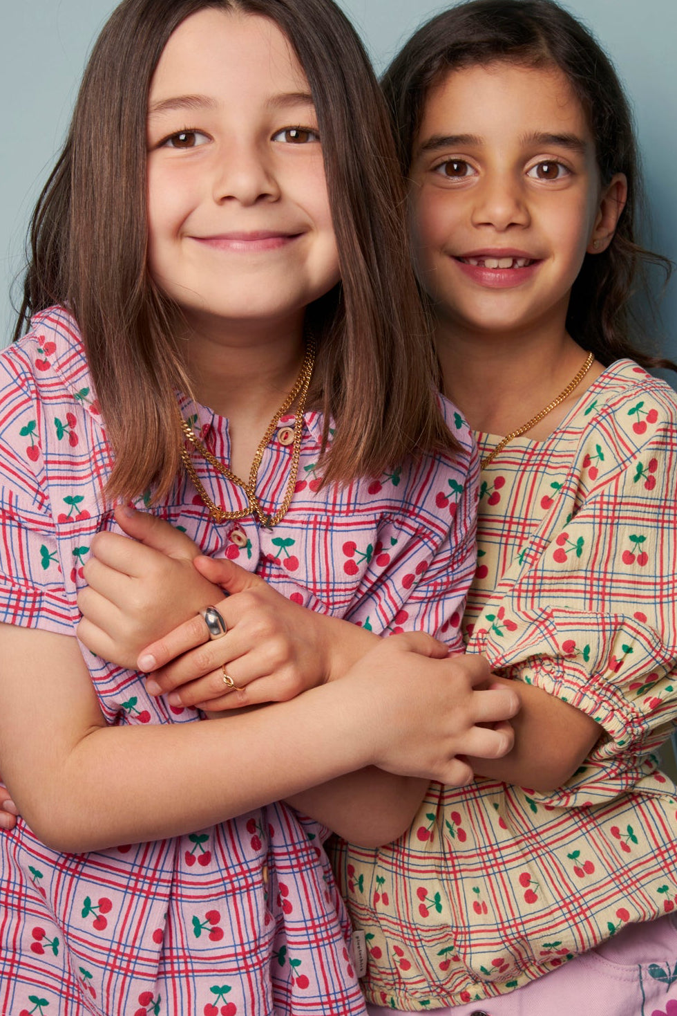 Two young girls wearing matching plaid outfits with cherry patterns.
