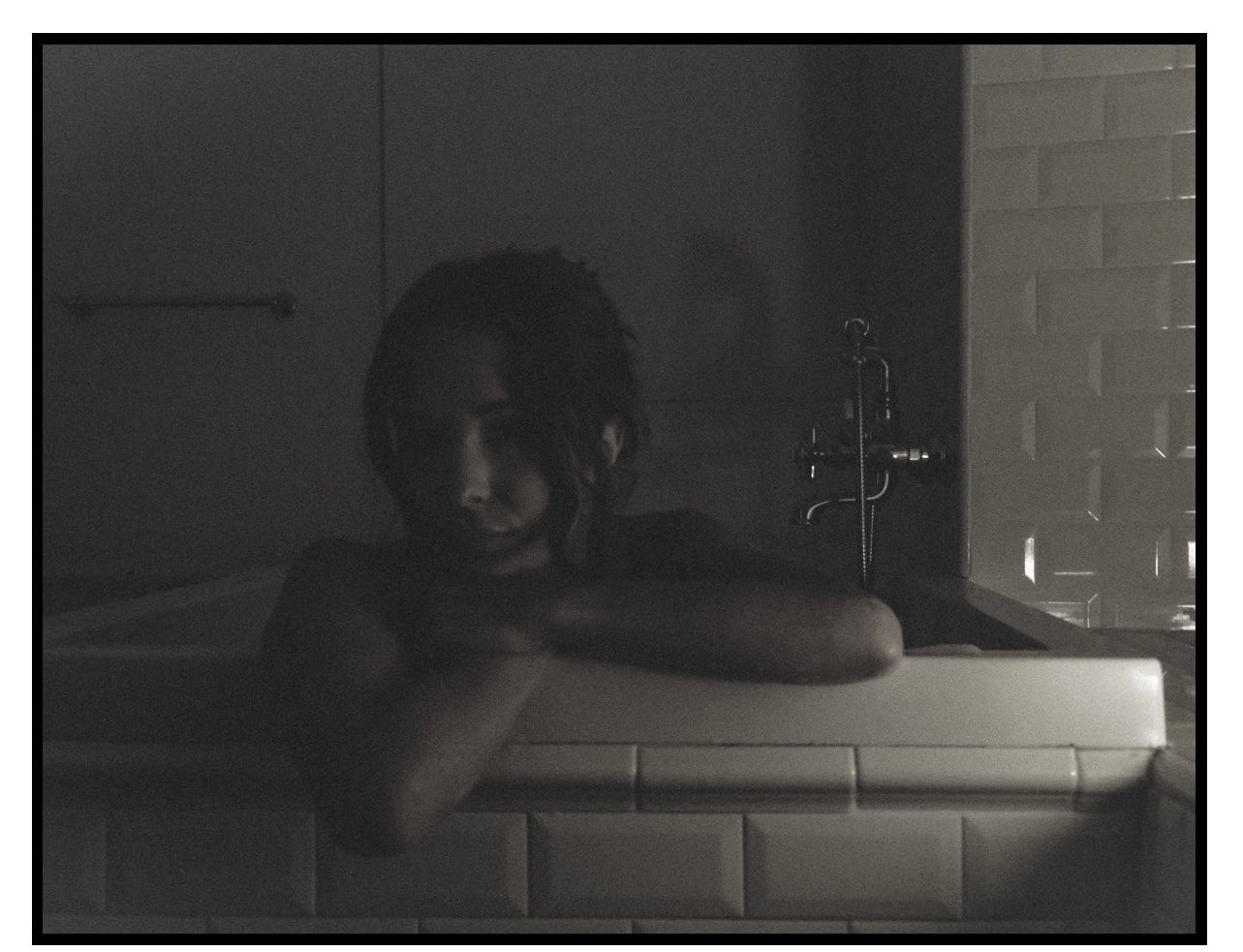 Person leaning over a bathtub in a dimly lit bathroom