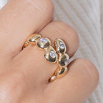 Gold ring with teardrop-shaped stones on a finger against a neutral background