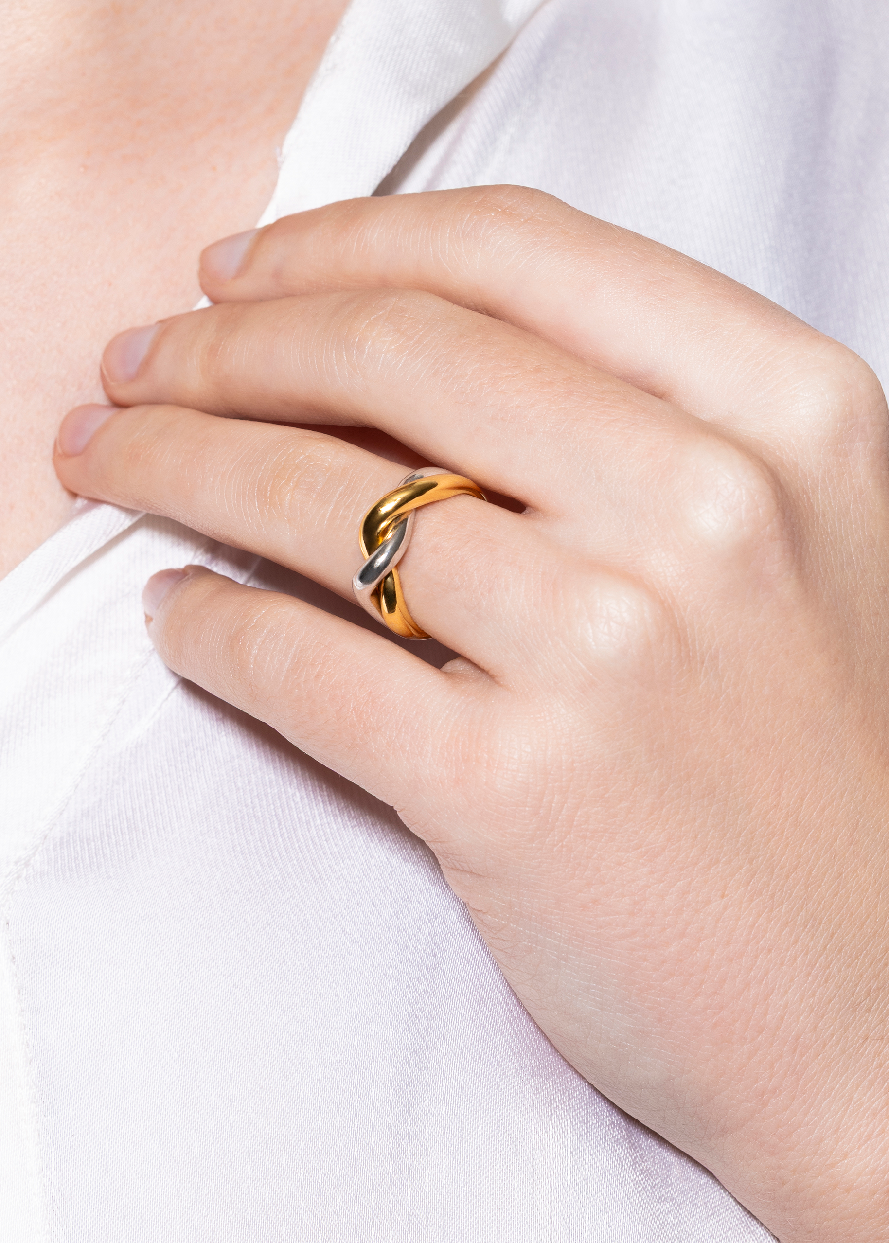 Gold and silver ring with a interwined detail on a person's finger against a white background
