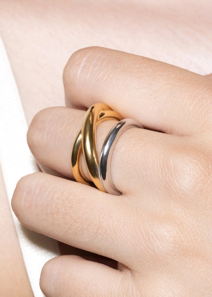 Close-up of a hand wearing a gold and silver ring on a light background